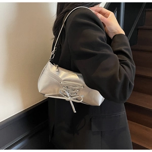 Close-up of a silver metallic baguette bag featuring a stylish bow on a black blazer