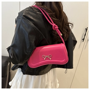 Close-up of rose pink shoulder bag featuring a gold metal bow and knotted strap detail