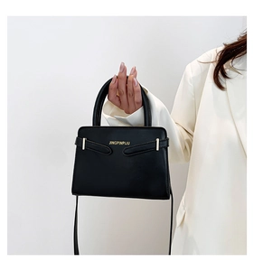 Detailopname van het gladde zwarte leren oppervlak met gouden gesp en logo op de handtas