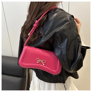 Side view of pink crossbody bag with gold bow clasp on elegant black and white outfit