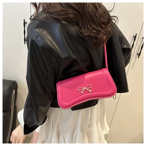 Detail of small rose red crossbody bag with golden bow decoration on black leather jacket