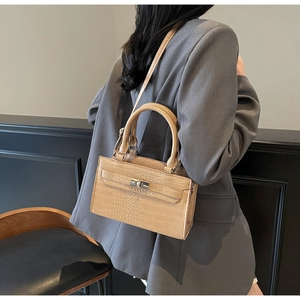 Detail of beige crocodile pattern handbag with metal twist lock worn by model