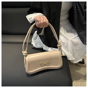 Close-up of cream bow clasp and unique knotted strap detail on leather handbag