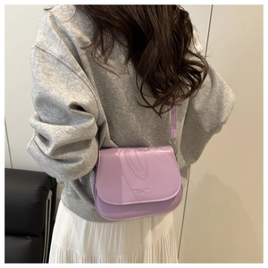 Detailed view of the light purple matte leather saddle bag worn as a crossbody by a model