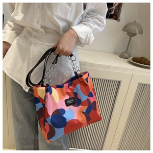 Detail of colorful geometric waterproof tote bag featuring metal chain handles and logo
