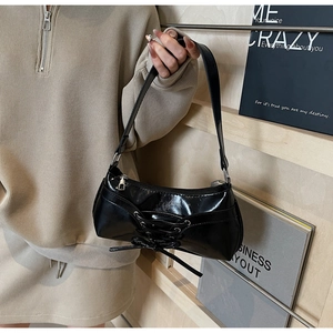 Detail of glossy black baguette bag featuring a ribbon bow and silver zipper closure