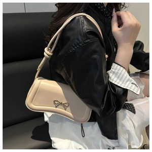 Close-up of beige crossbody bag with golden bow hardware and knotted strap details