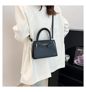 Détail d'un sac à main trapèze en cuir noir avec logo doré sur un blazer blanc