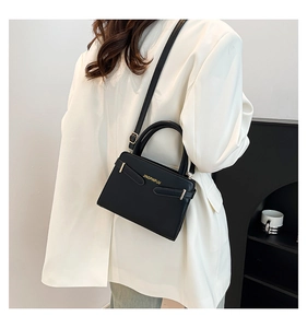 Vue latérale du sac à bandoulière en similicuir noir porté sur un blazer blanc