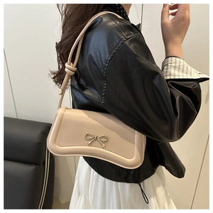 Detail of beige PU leather crossbody bag with a gold bow buckle and knotted strap