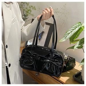 Close-up of glossy black shoulder bag featuring pleated front pockets and bow details