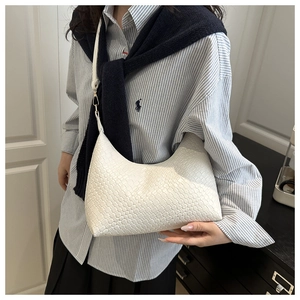 Close-up of a white woven PU underarm bag being held by a model in a trendy outfit