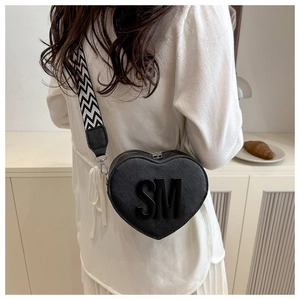 Detail of heart-shaped black crossbody bag featuring 3D letters and chevron wide strap