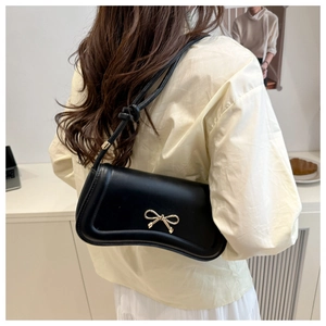 Detail of a black leather handbag with a delicate gold bow buckle worn on the shoulder
