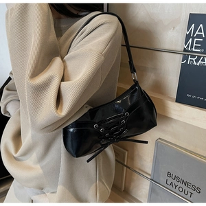 Detail of black glossy shoulder bag featuring distinctive corset-style lacing on the front