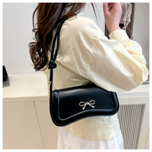 Side view of black faux leather crossbody bag with golden bow hardware on model