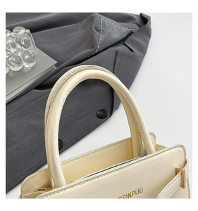 Détail du sac en cuir crème avec poignée incurvée et finitions dorées élégantes
