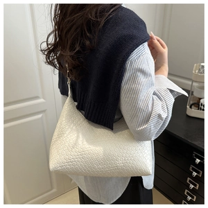 A white woven PU leather underarm bag shown worn by a model in a stylish casual outfit