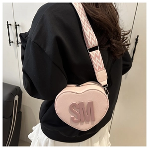 Pink heart-shaped crossbody bag with SM logo and striped wide strap shown on model