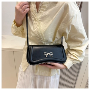 Detail of matte black leather bag featuring a gold bow buckle and slender shoulder strap