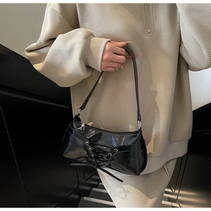Detailed view of black patent leather baguette bag with silver eyelet lace-up design