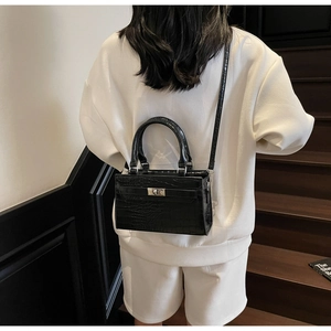 Detail of black crocodile texture bag with silver twist lock on a white outfit