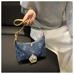Detail of a denim shoulder bag with bear prints, yellow straps and a cream cup charm