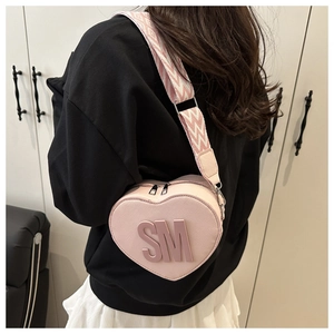 Close-up of pink heart-shaped crossbody bag with SM logo and textured wide strap