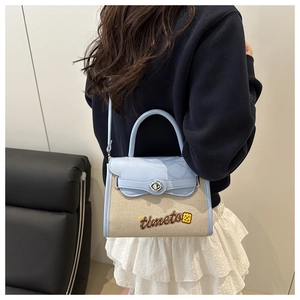 Model wearing a beige canvas and blue leather crossbody bag with floral embroidery