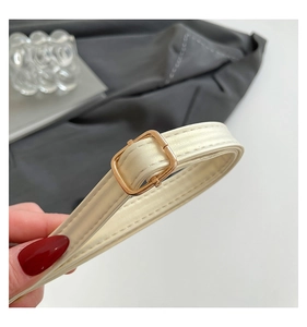 Gros plan d'une bandoulière en cuir crème avec boucle dorée et coutures de précision