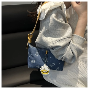 Detail of denim underarm bag with bear prints and a cupcake charm on a shoulder strap