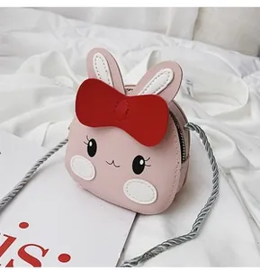 Detail of pink rabbit shoulder bag with red bow and grey twisted rope strap on white bed