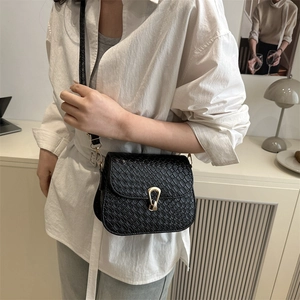 Chic black crossbody bag with woven texture and gold horseshoe buckle on white shirt