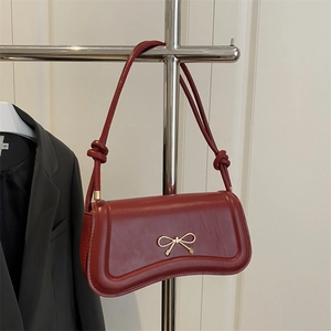 Deep red bow leather crossbody bag with gold buckle hung on a metal rack