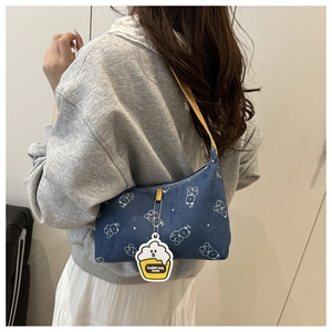 Detail of dark blue denim shoulder bag with white bear print and yellow charm