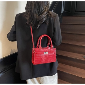 Detail of red crocodile texture handbag with silver twist lock on female model