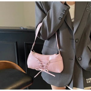 Detail of pink glossy leather underarm bag featuring a trendy front lace-up bow design