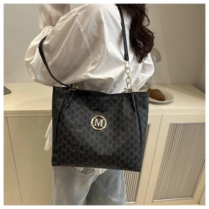 Detail of vintage patterned tote bag with gold M logo and chain strap on female model