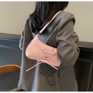 Close-up of pink pleated shoulder bag with ribbon lacing details on grey blazer