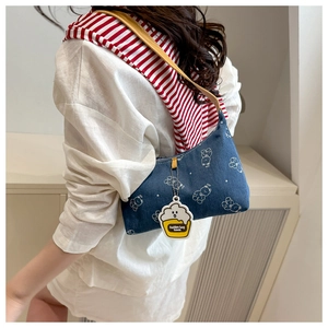Detail of blue denim shoulder bag with white bear prints and a yellow cupcake charm