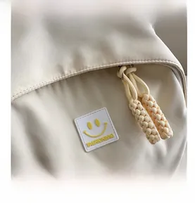 Macro detail of cream backpack with fashion smile badge and woven zipper puller