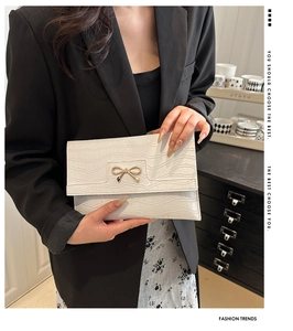 Detail of white crocodile texture envelope bag with elegant golden bow buckle feature