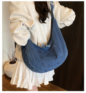 Detail of blue denim hobo bag featuring functional side pocket and frayed zipper trim