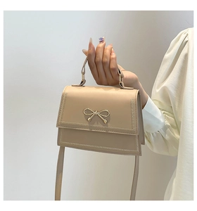 Vista detallada de un elegante bolso beige con lazo dorado y costuras decorativas.