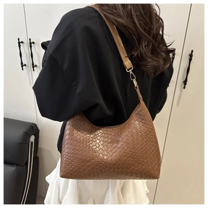 Detail of a brown woven PU leather shoulder bag worn on the shoulder by a model
