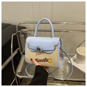 Detail of blue leather and beige canvas handbag with smiling face embroidery and lock