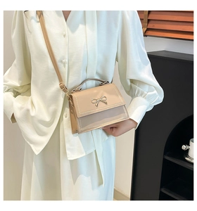 Bolso bandolera beige elegante con lazo metálico, llevado por una modelo con luz suave.