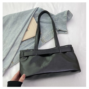 Detail of glossy black shoulder bag with decorative buckle and slim straps on denim jacket