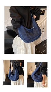 Detail view of a large navy denim crescent tote bag with outer pocket and zipper closure