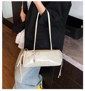 Detail of cream underarm bag with pearl bow pendant and soft synthetic leather texture